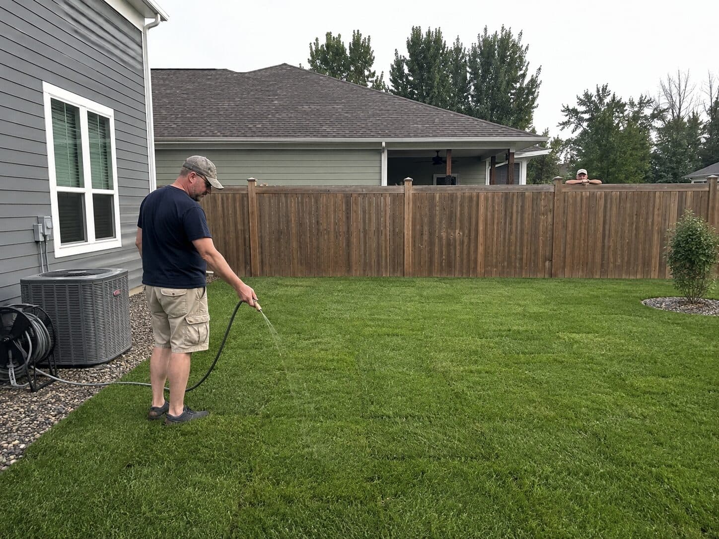 Homeowner watering a lush backyard lawn with a garden hose
