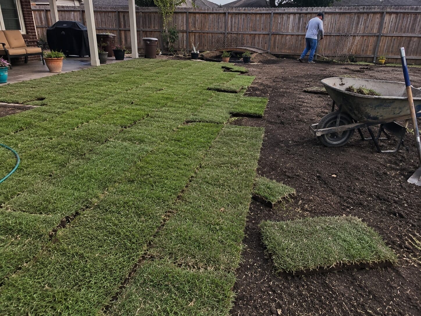 Backyard sod installation in progress beside prepared soil